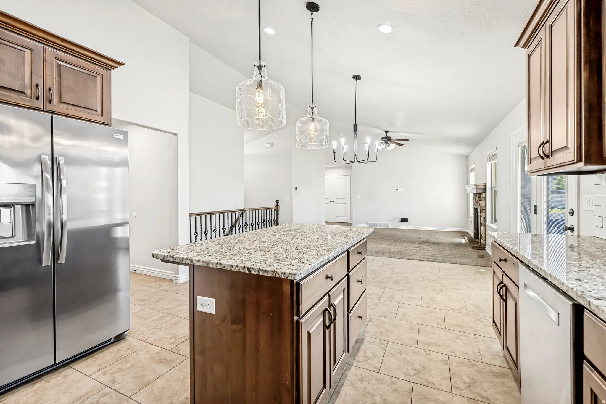 Kitchen featuring stainless steel appliances, open floor plan, light stone countertops, vaulted ceiling, and a kitchen island
