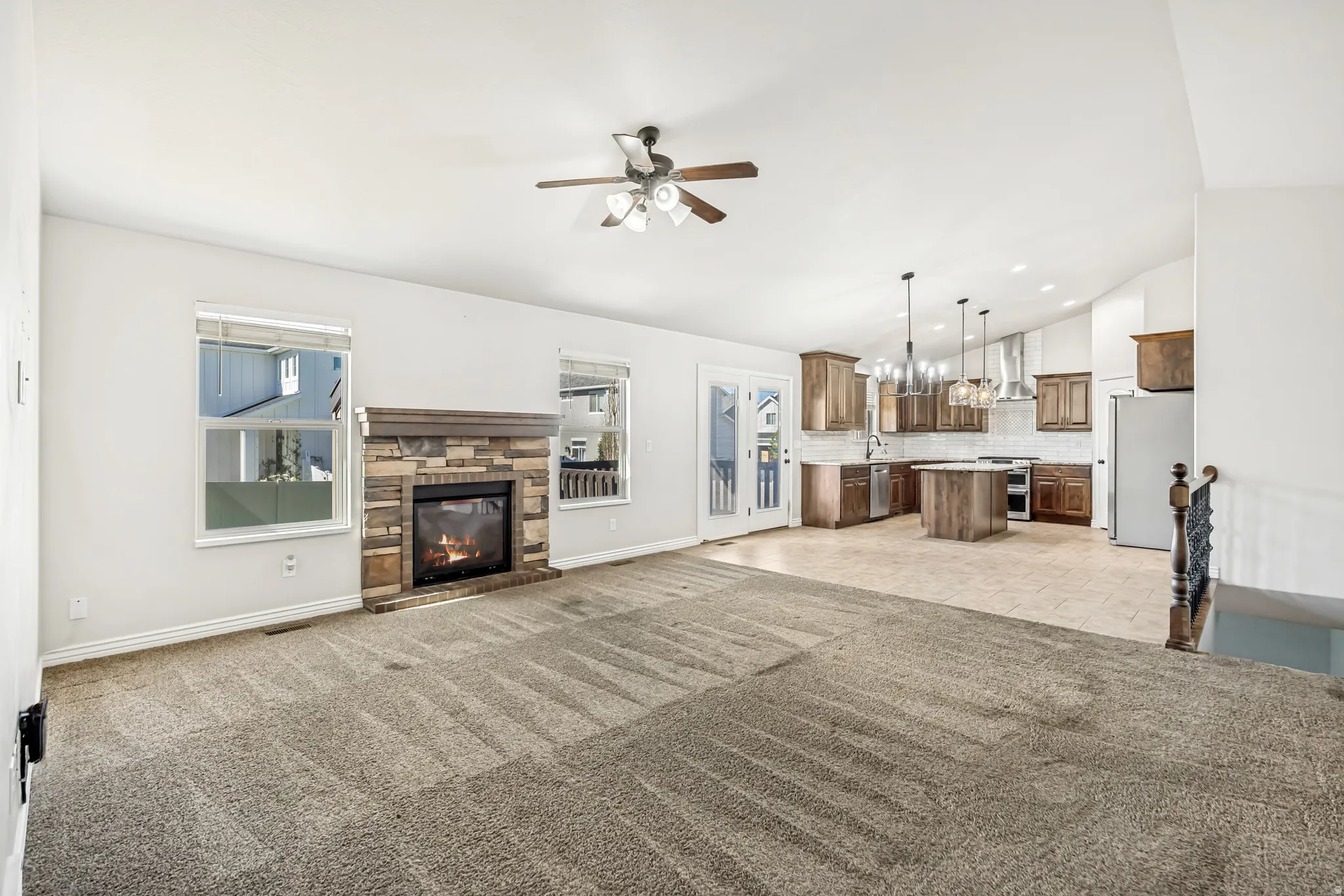 Unfurnished living room featuring ceiling fan, vaulted ceiling, a fireplace, light carpet, and a chandelier
