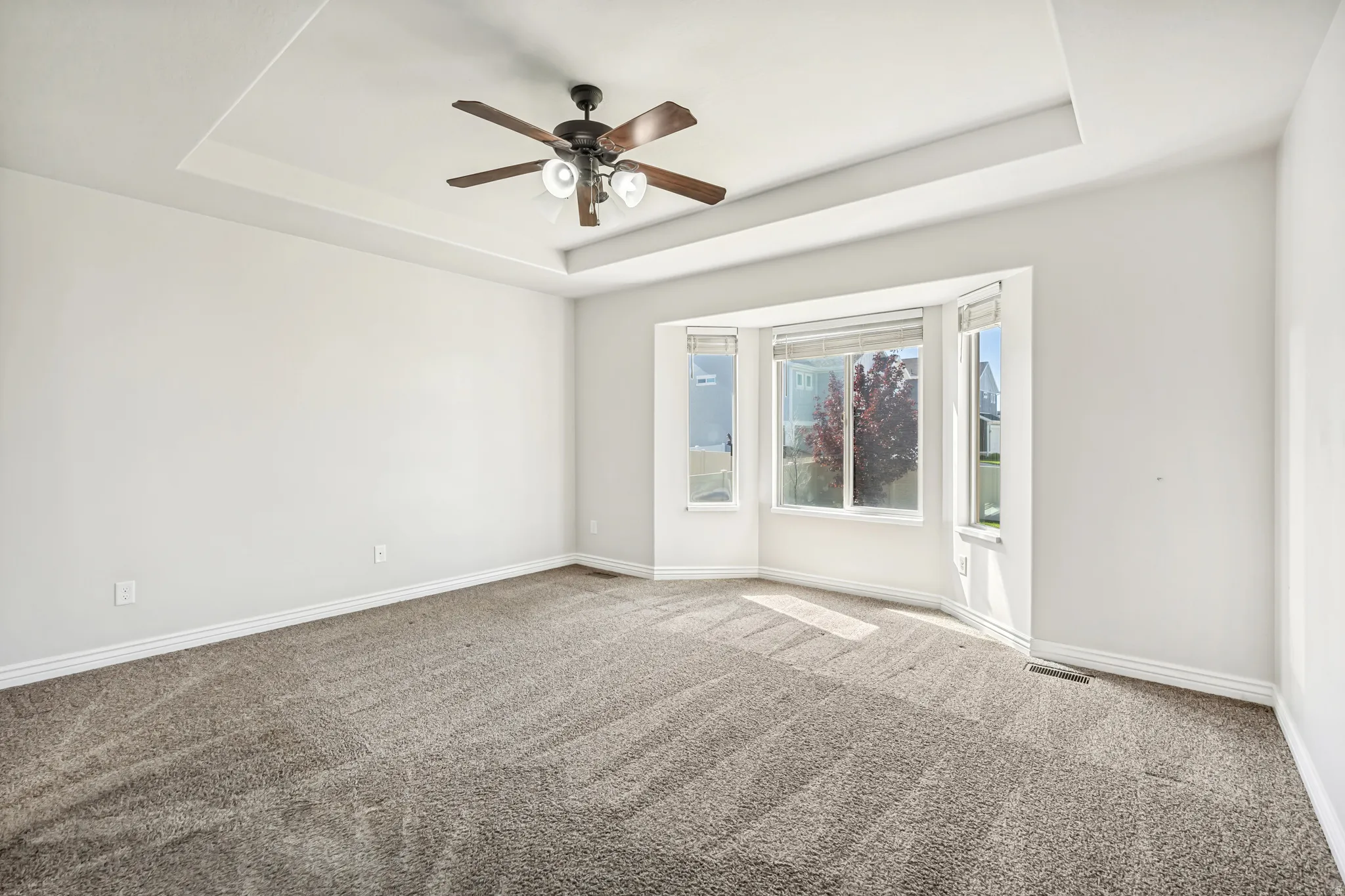 Unfurnished room featuring ceiling fan, light colored carpet, and a raised ceiling