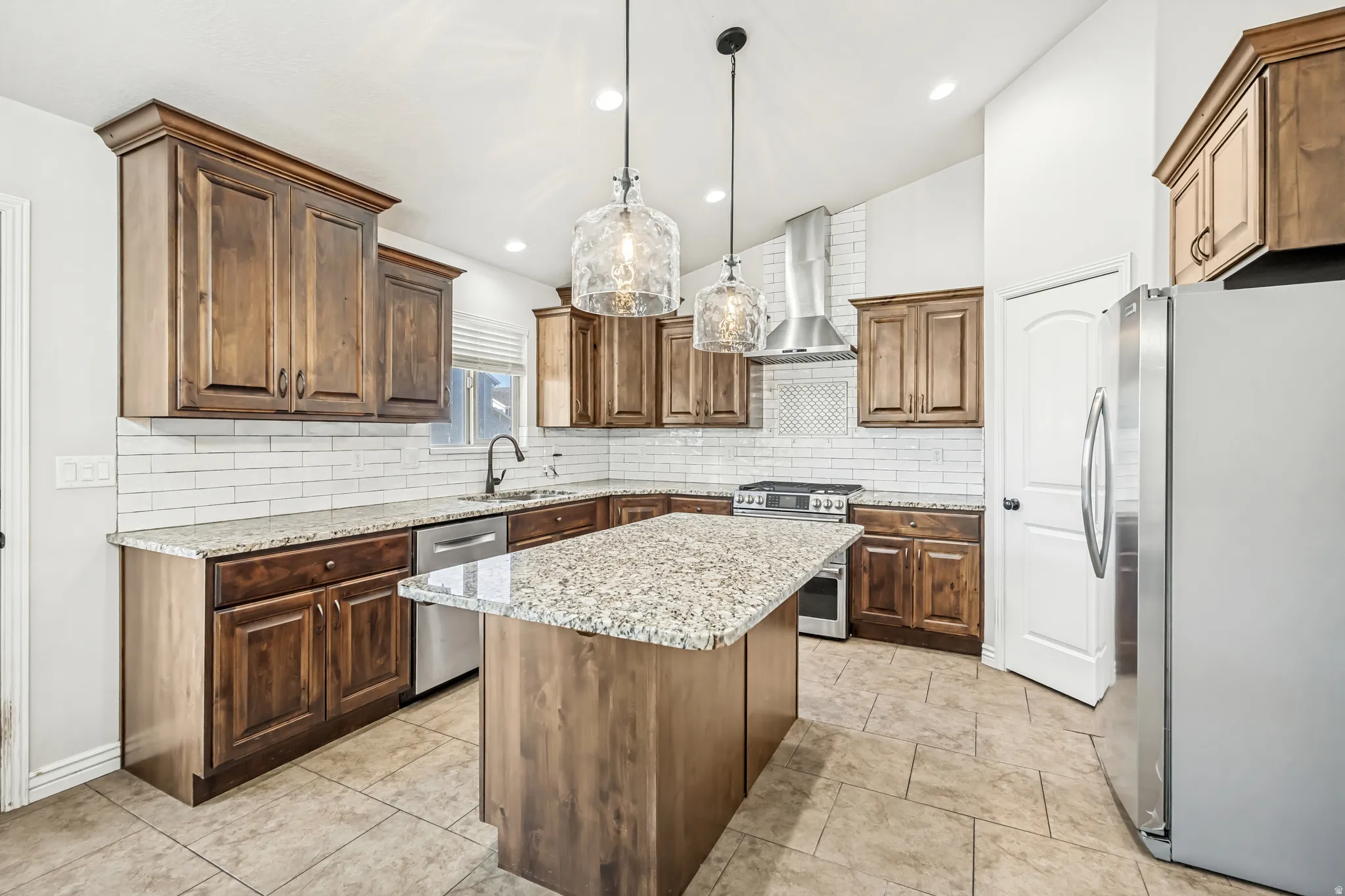 Kitchen with stainless steel appliances, a kitchen island, light stone countertops, pendant lighting, and tasteful backsplash