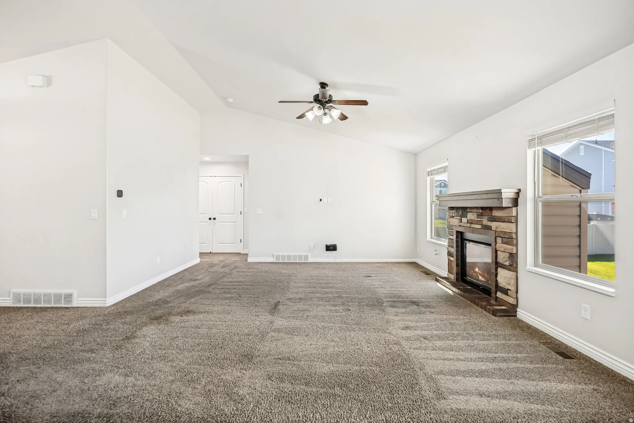 Unfurnished living room with dark colored carpet, a ceiling fan, a fireplace, and vaulted ceiling