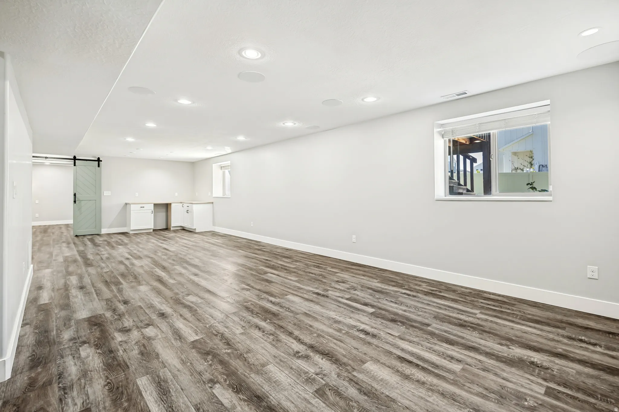 Unfurnished living room with dark wood finished floors, a barn door, built in study area, and recessed lighting