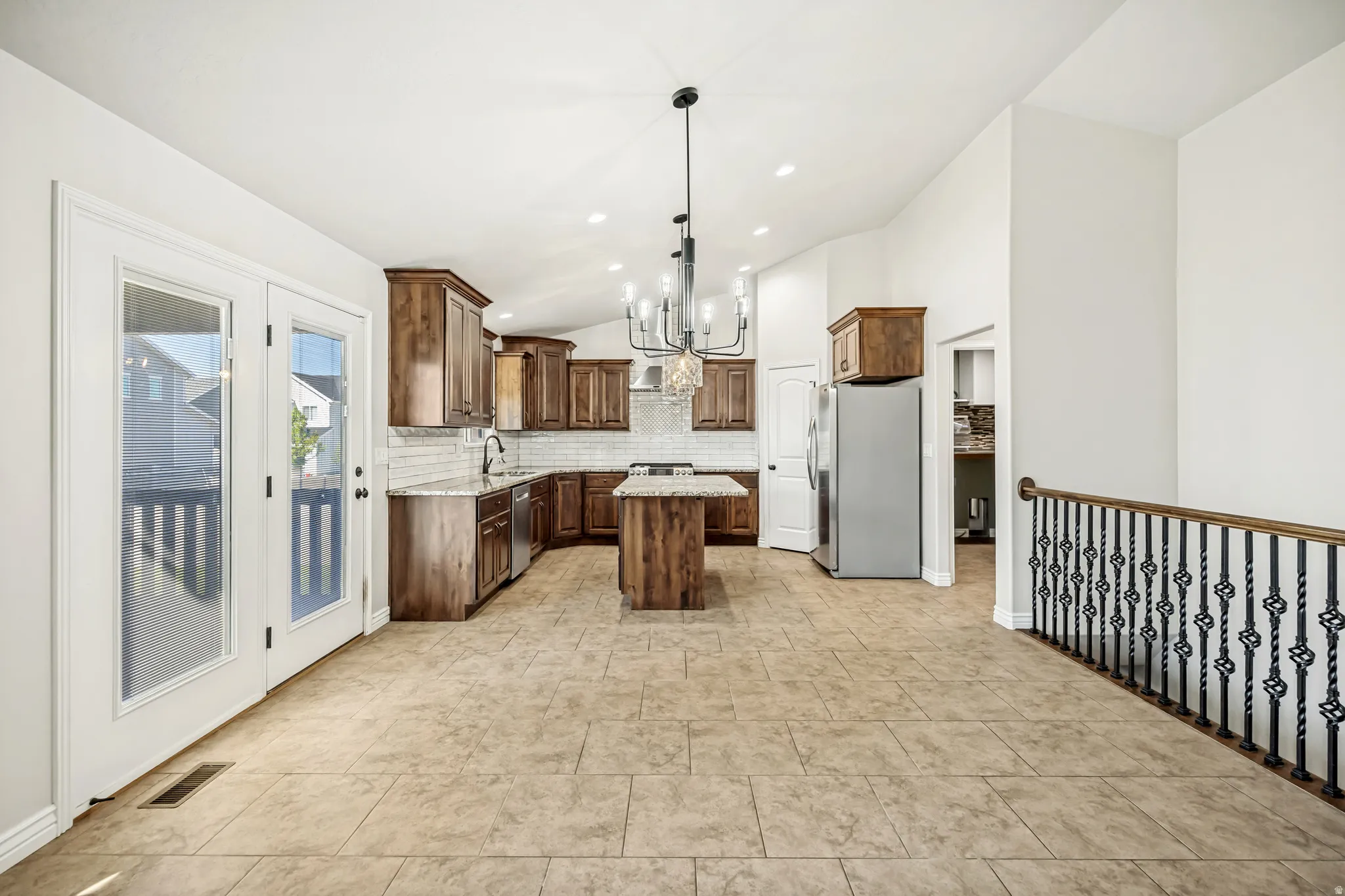 Kitchen featuring a center island, backsplash, a chandelier, stainless steel appliances, and lofted ceiling