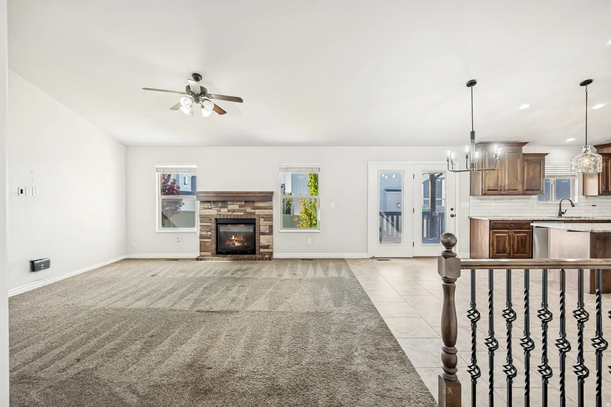Unfurnished living room with hanging lights, a stone fireplace, light tile patterned flooring, and ceiling fan