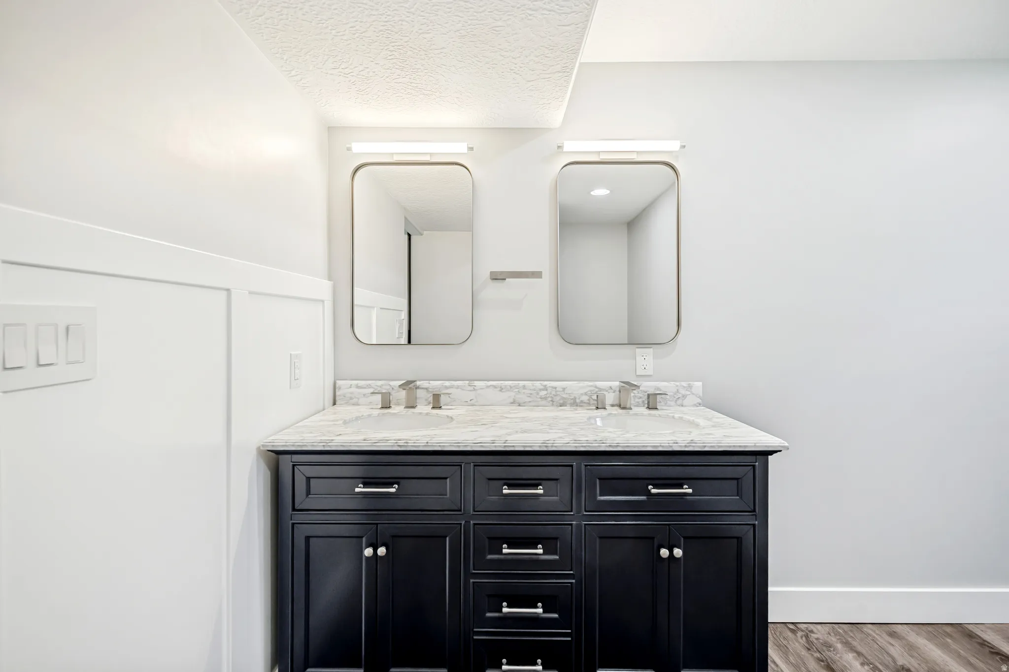 Bathroom featuring double vanity, wood finished floors, and a textured ceiling