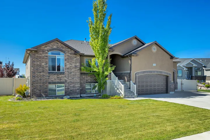 View of front facade with concrete driveway, stucco siding, an attached garage, brick siding, and a gate