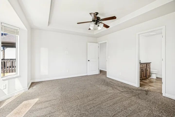 Unfurnished bedroom with dark colored carpet, a raised ceiling, connected bathroom, and ceiling fan