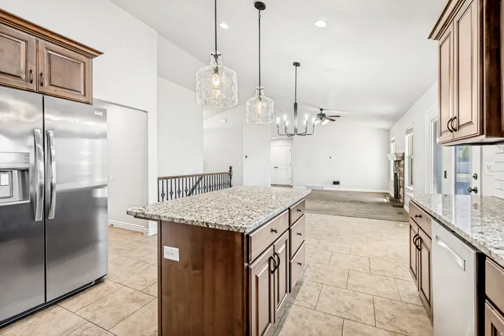 Kitchen featuring stainless steel appliances, open floor plan, light stone countertops, vaulted ceiling, and a kitchen island