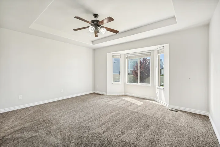 Unfurnished room featuring ceiling fan, light colored carpet, and a raised ceiling