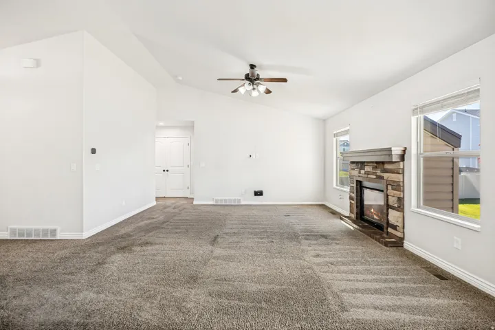 Unfurnished living room with dark colored carpet, a ceiling fan, a fireplace, and vaulted ceiling