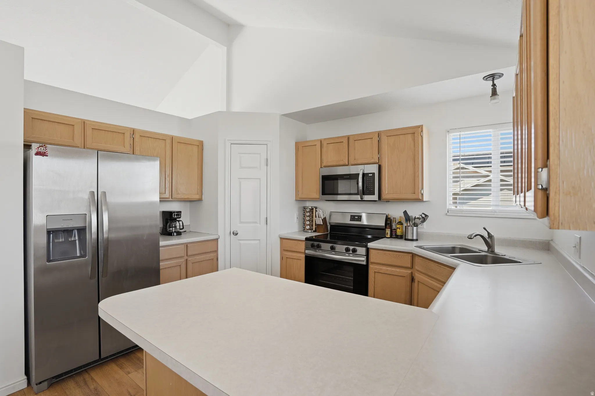 Kitchen with stainless steel appliances, light countertops, a peninsula, light wood-style floors, and light wood finish cabinets