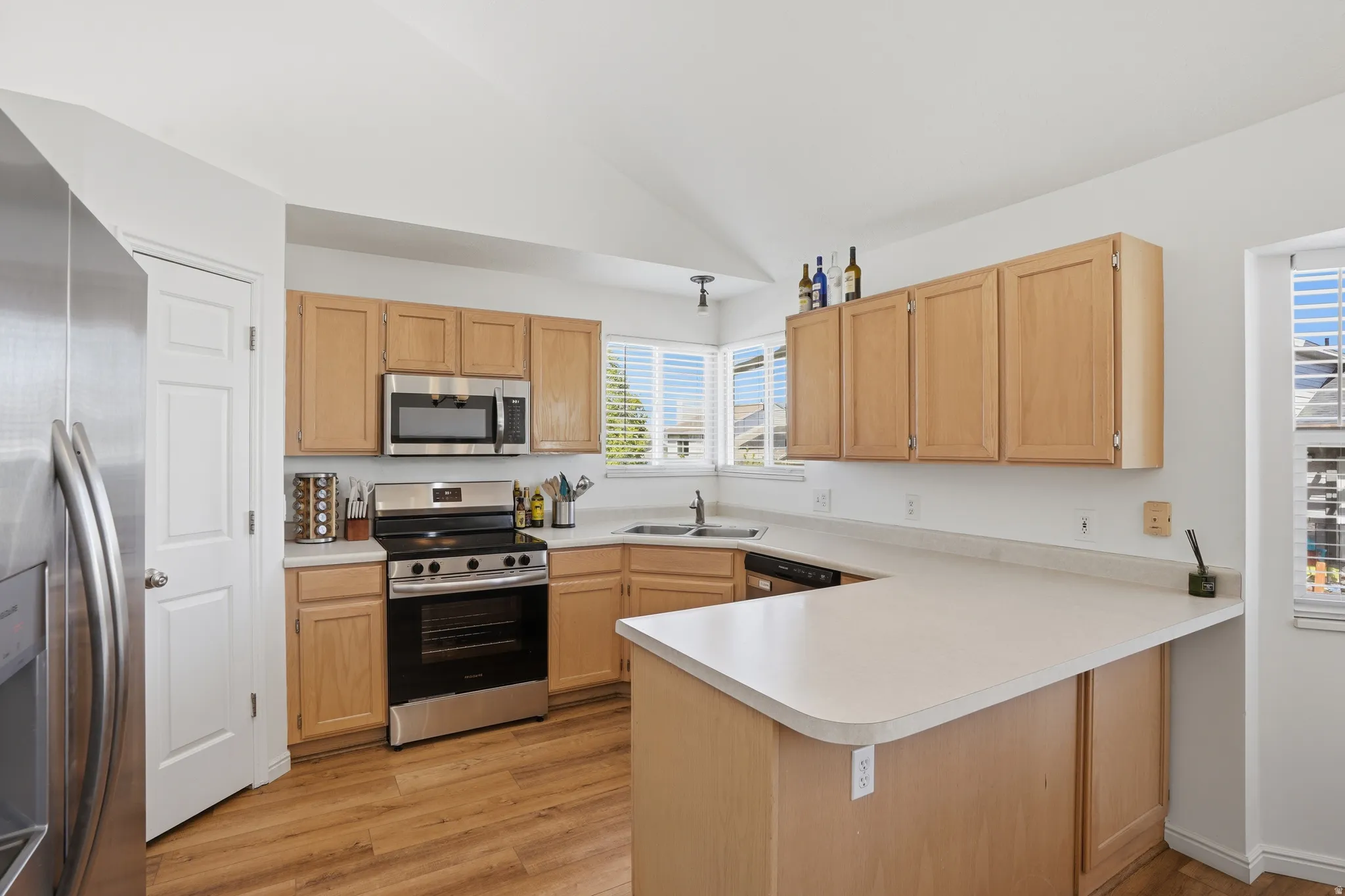 Kitchen featuring a peninsula, stainless steel appliances, light wood finish cabinets, vaulted ceiling, and light countertops