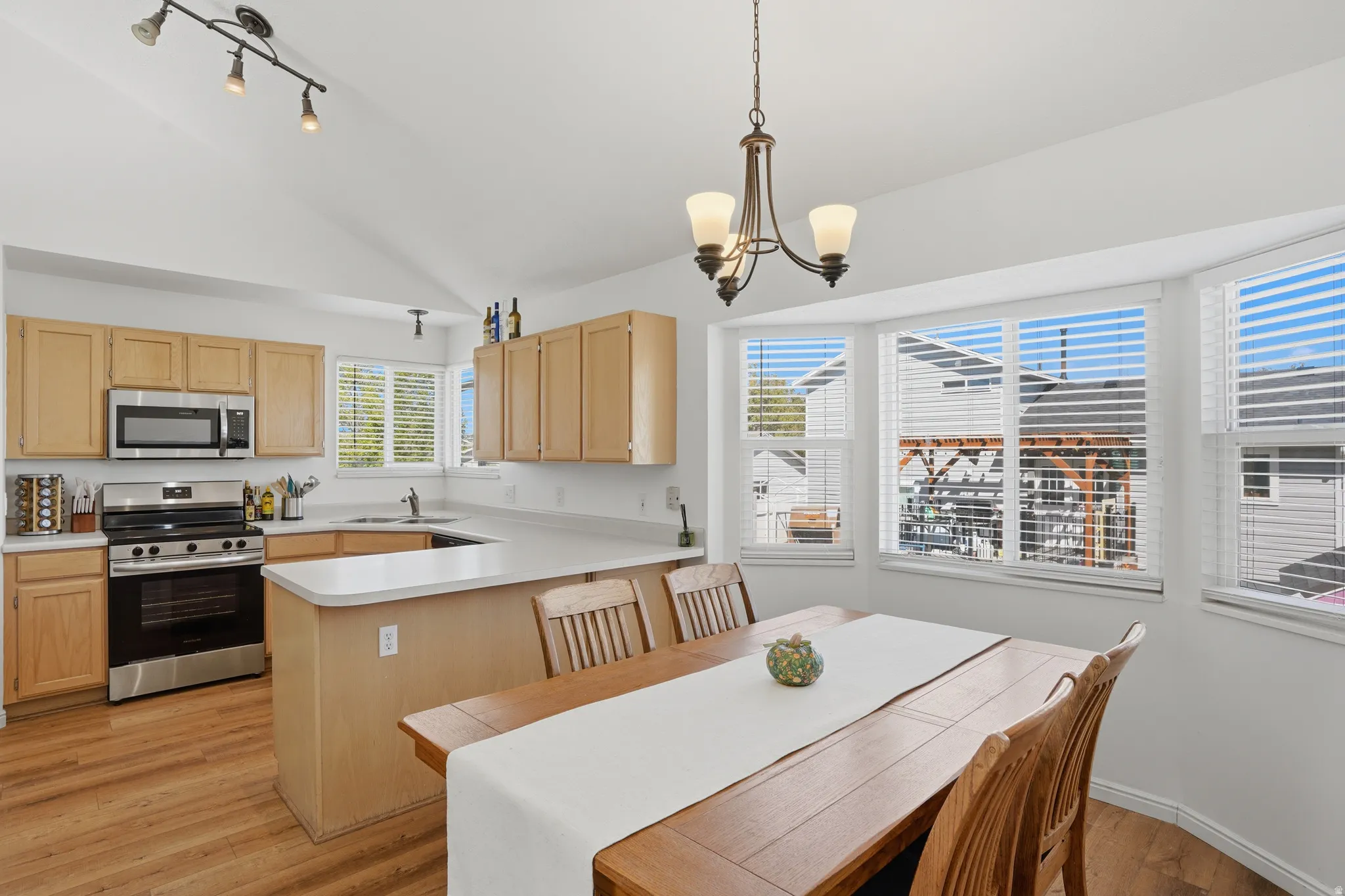 Kitchen featuring light wood finish cabinetry, stainless steel appliances, light countertops, a peninsula, and light wood finished floors