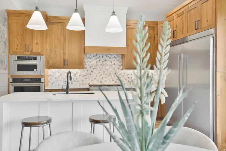 Kitchen featuring stainless steel appliances, a breakfast bar area, light stone counters, decorative light fixtures, and an island with sink