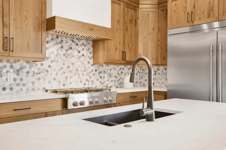 Kitchen with stainless steel appliances, light stone countertops, backsplash, and wood finish cabinets