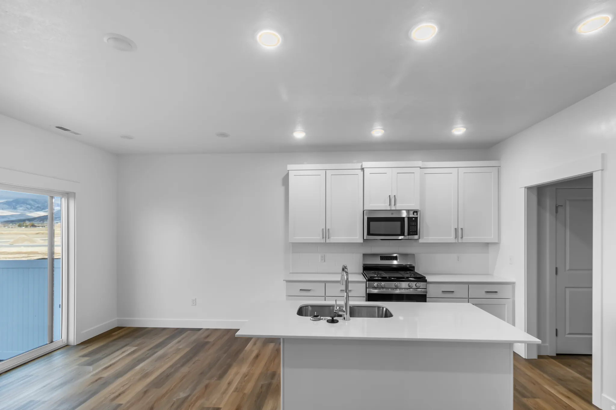 Kitchen featuring dark wood-style floors, white cabinets, stainless steel appliances, a kitchen island with sink, and light stone counters