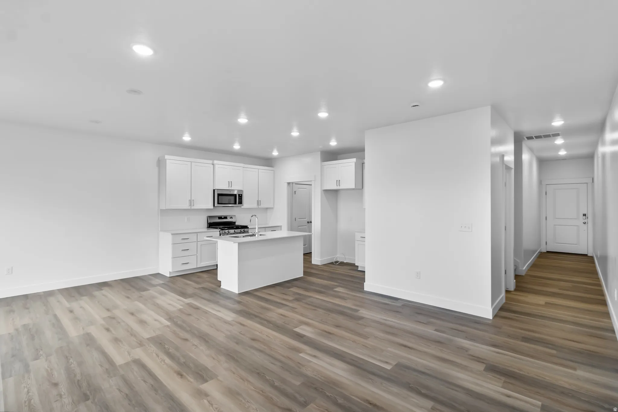 Kitchen featuring white cabinets, an island with sink, light wood-type flooring, recessed lighting, and stainless steel appliances