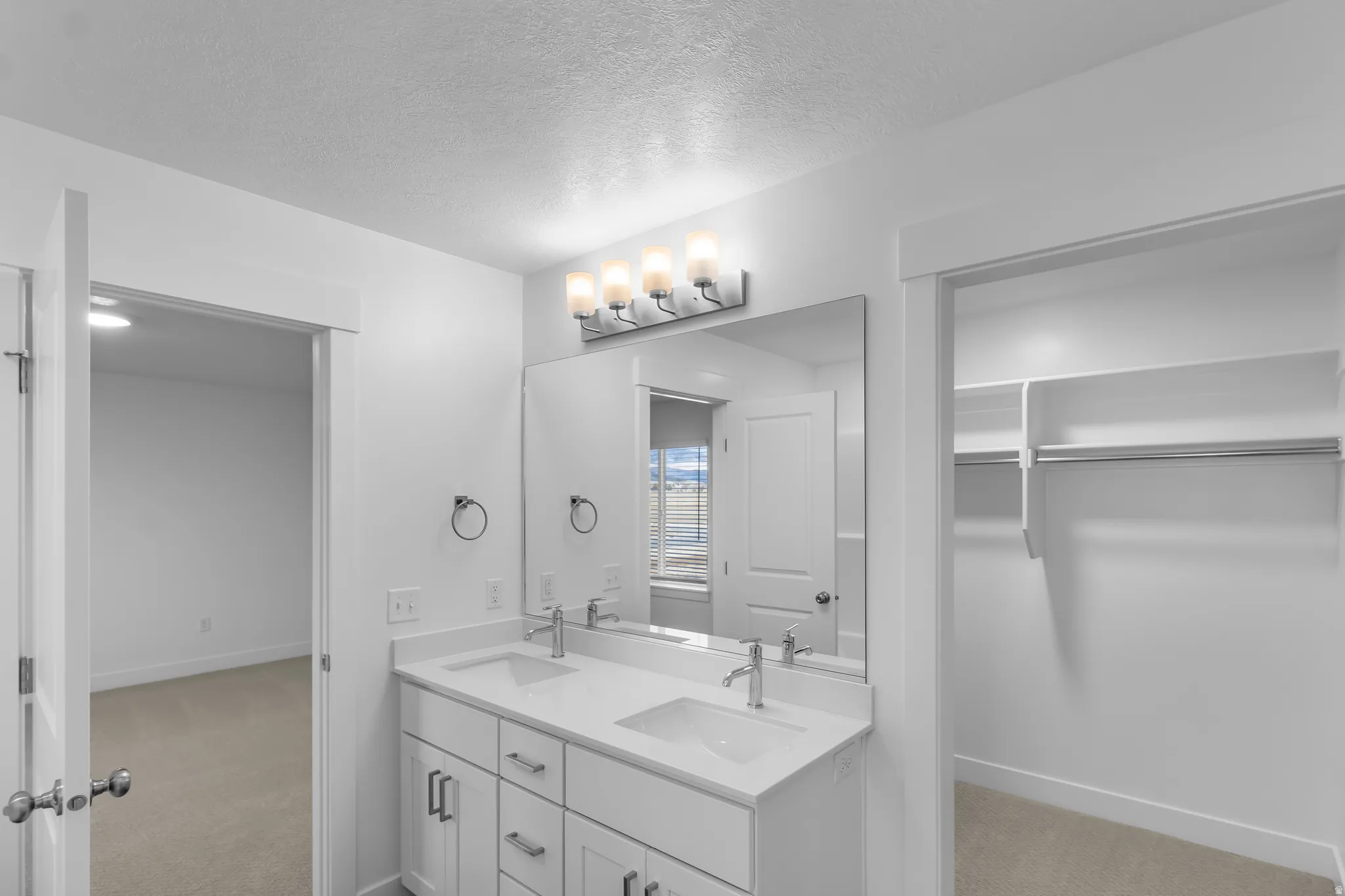 Full bathroom featuring a walk in closet, double vanity, light carpet, and a textured ceiling