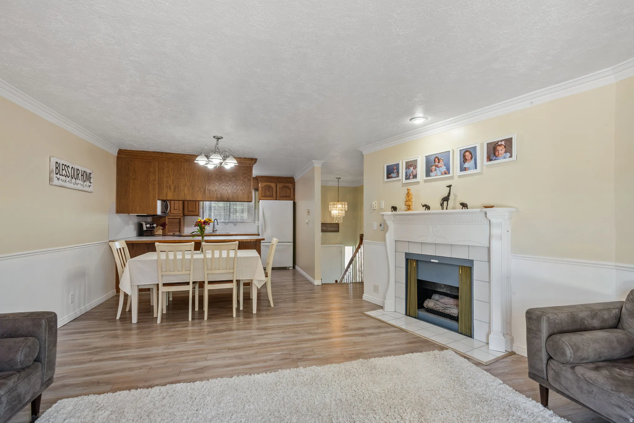 Dining area featuring light wood-style floors, a tile fireplace, hanging lights, crown molding, and a textured ceiling