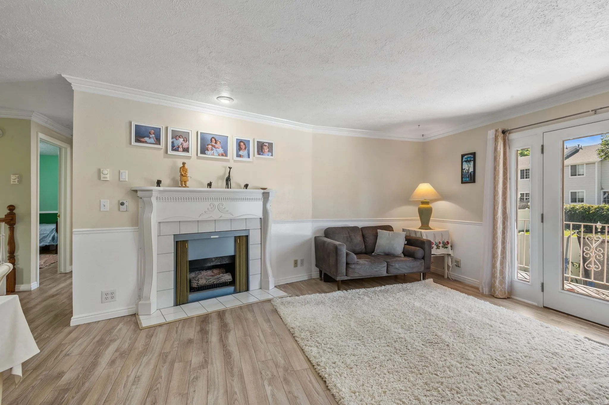 Living area with light wood-type flooring, crown molding, a fireplace, a textured ceiling, and wainscoting
