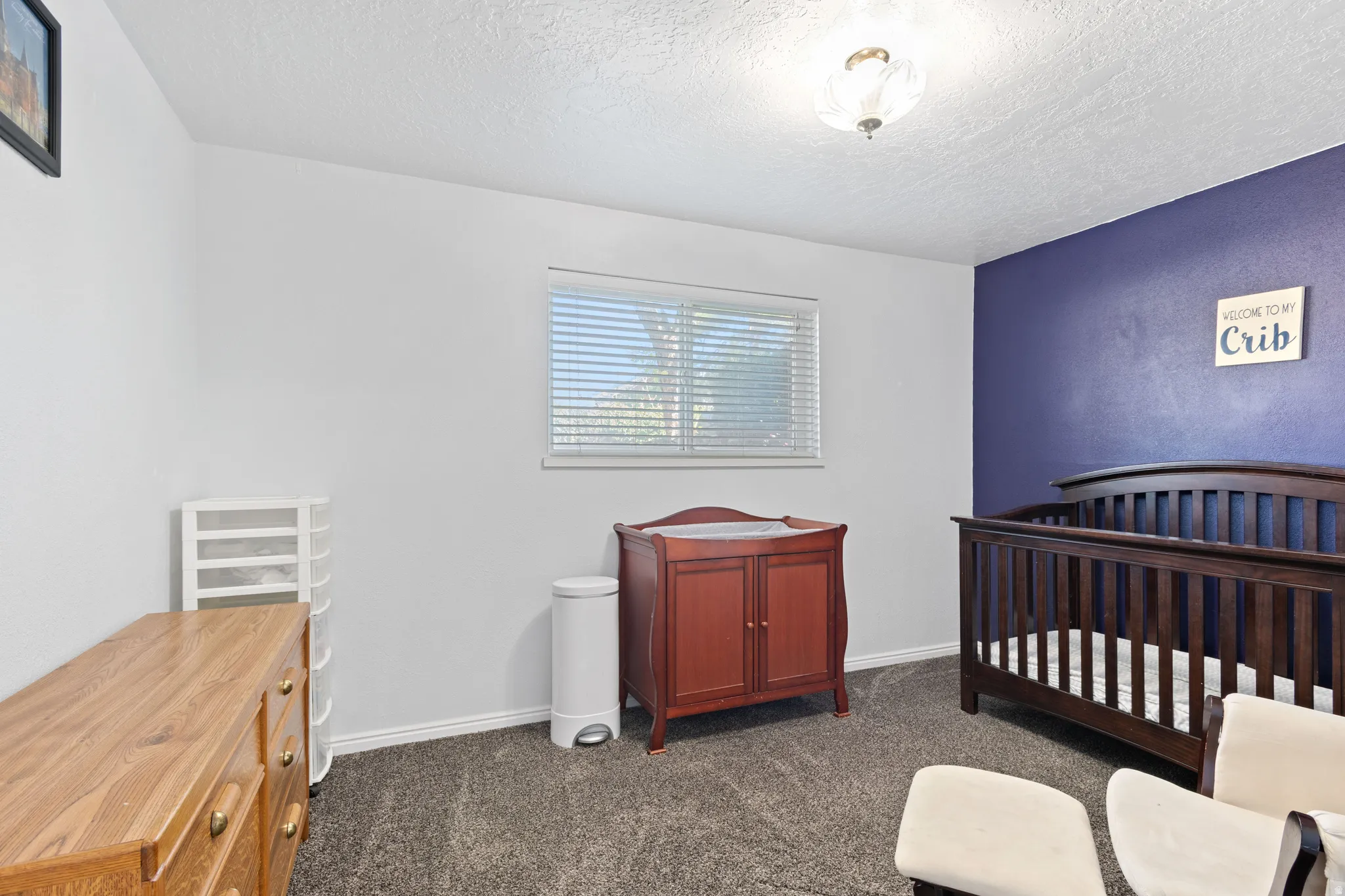 Bedroom featuring a crib, dark carpet, and a textured ceiling