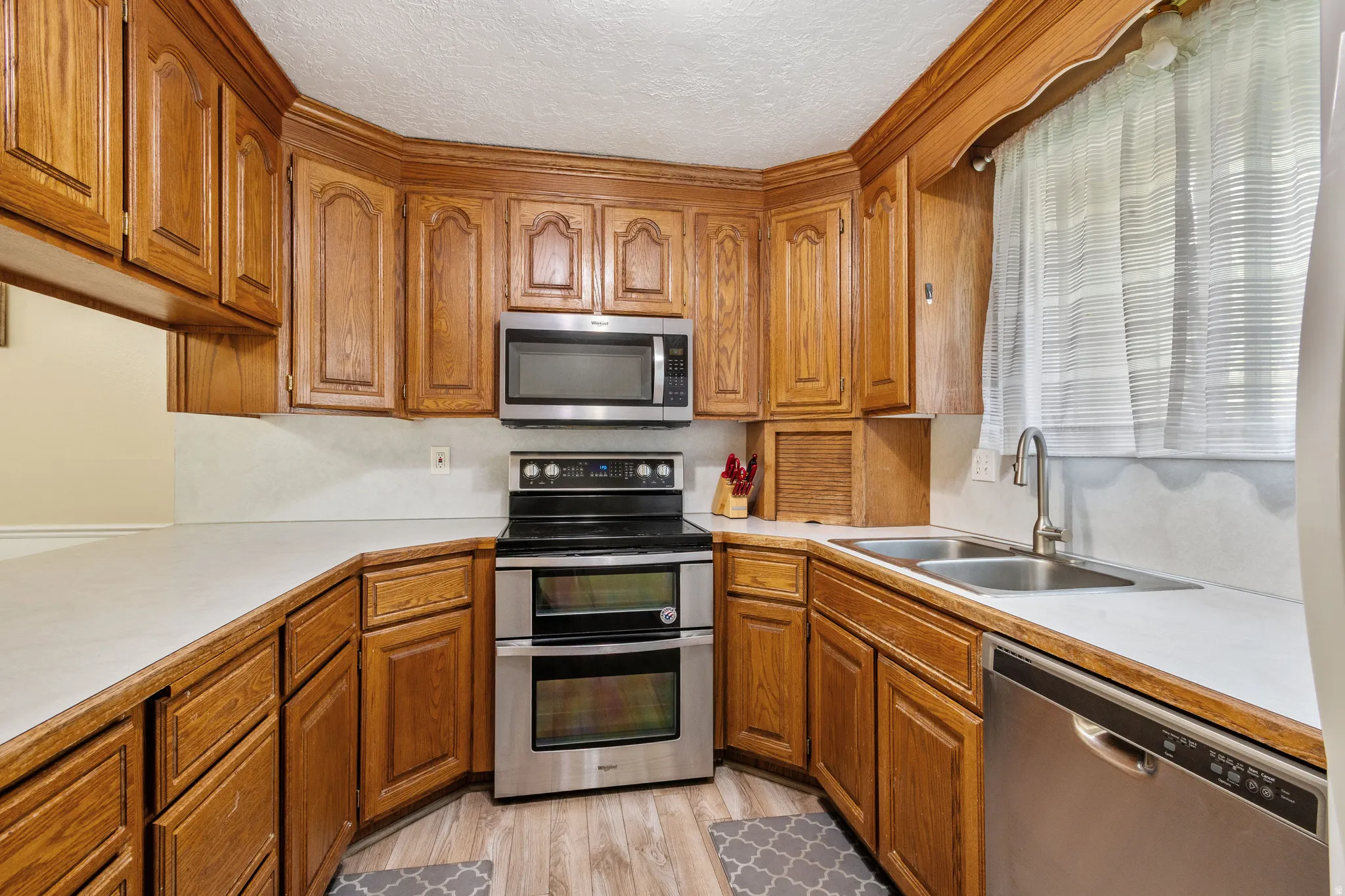 Kitchen with light countertops, wood finish cabinetry, stainless steel appliances, a textured ceiling, and light wood finished floors