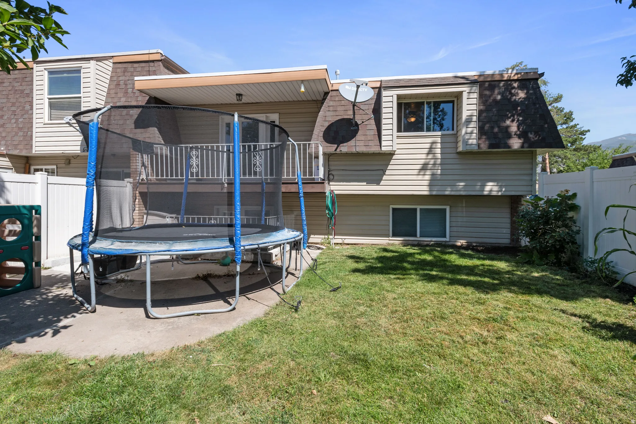 Rear view of property featuring mansard roof, a trampoline, a shingled roof, and a patio area