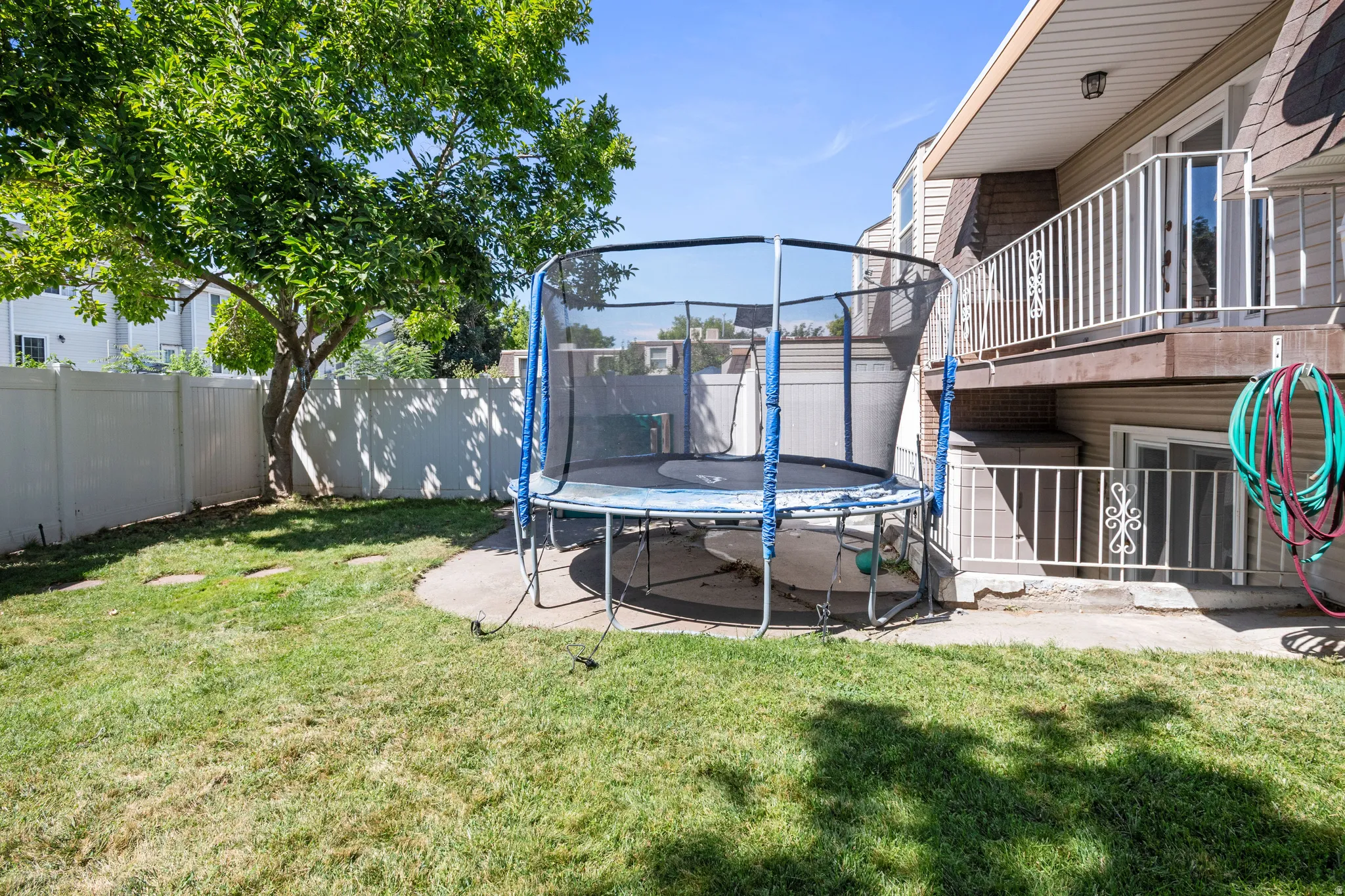 Fenced backyard featuring a trampoline and a patio area