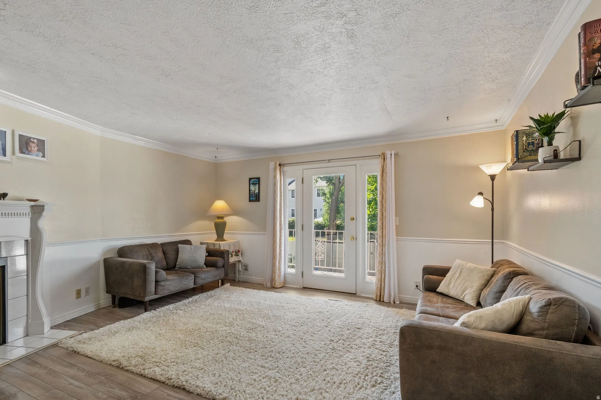 Living room featuring light wood-type flooring, crown molding, a textured ceiling, and a tiled fireplace