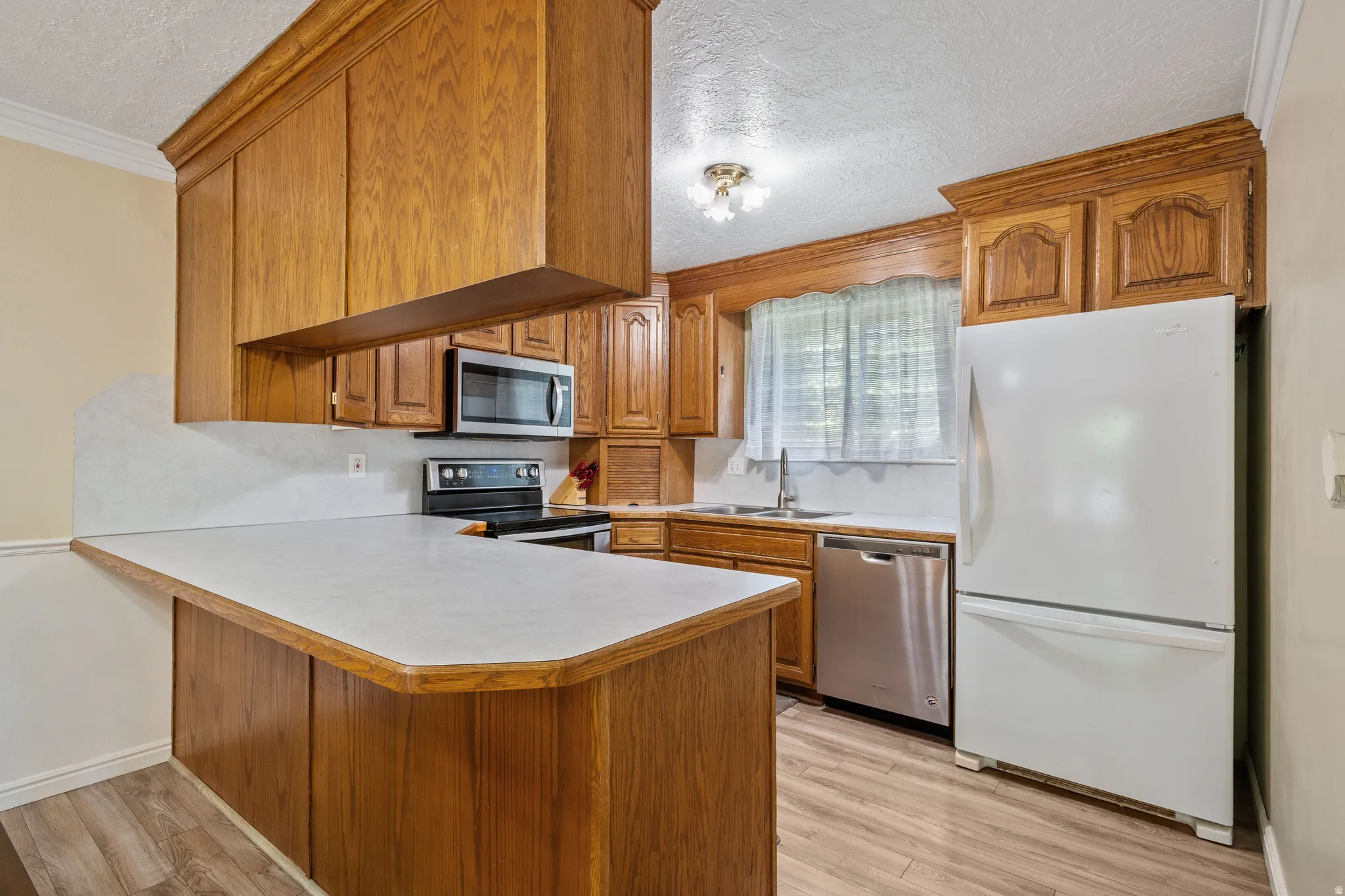 Kitchen featuring wood finish cabinetry, stainless steel appliances, a textured ceiling, light countertops, and a peninsula