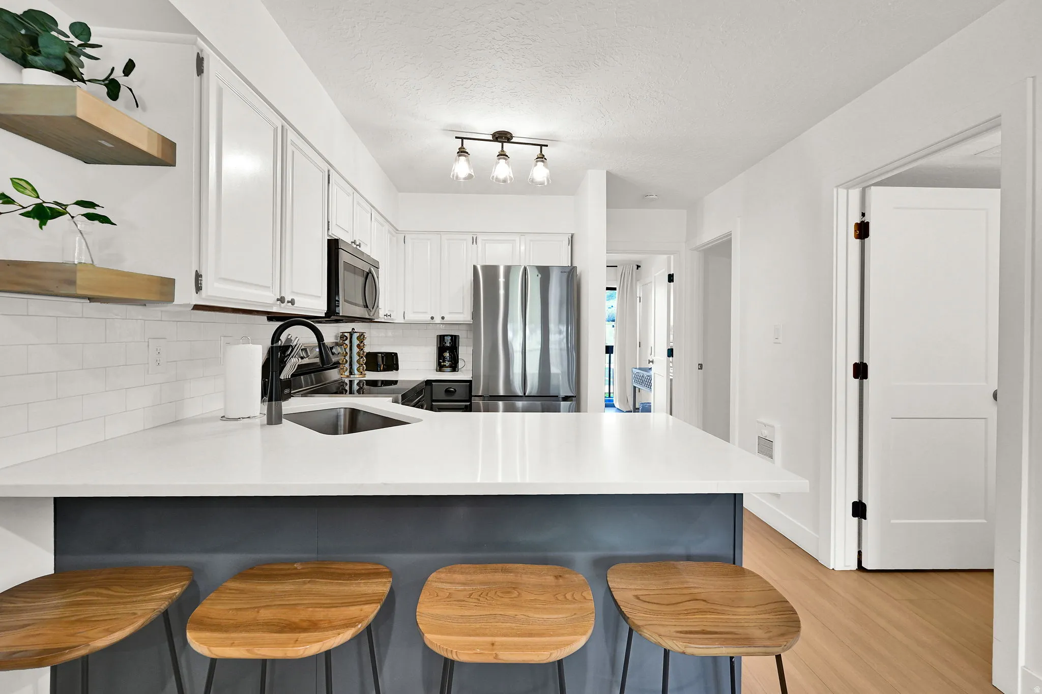 Kitchen featuring a peninsula, a breakfast bar, open shelves, stainless steel appliances, and two-tone cabinets.
