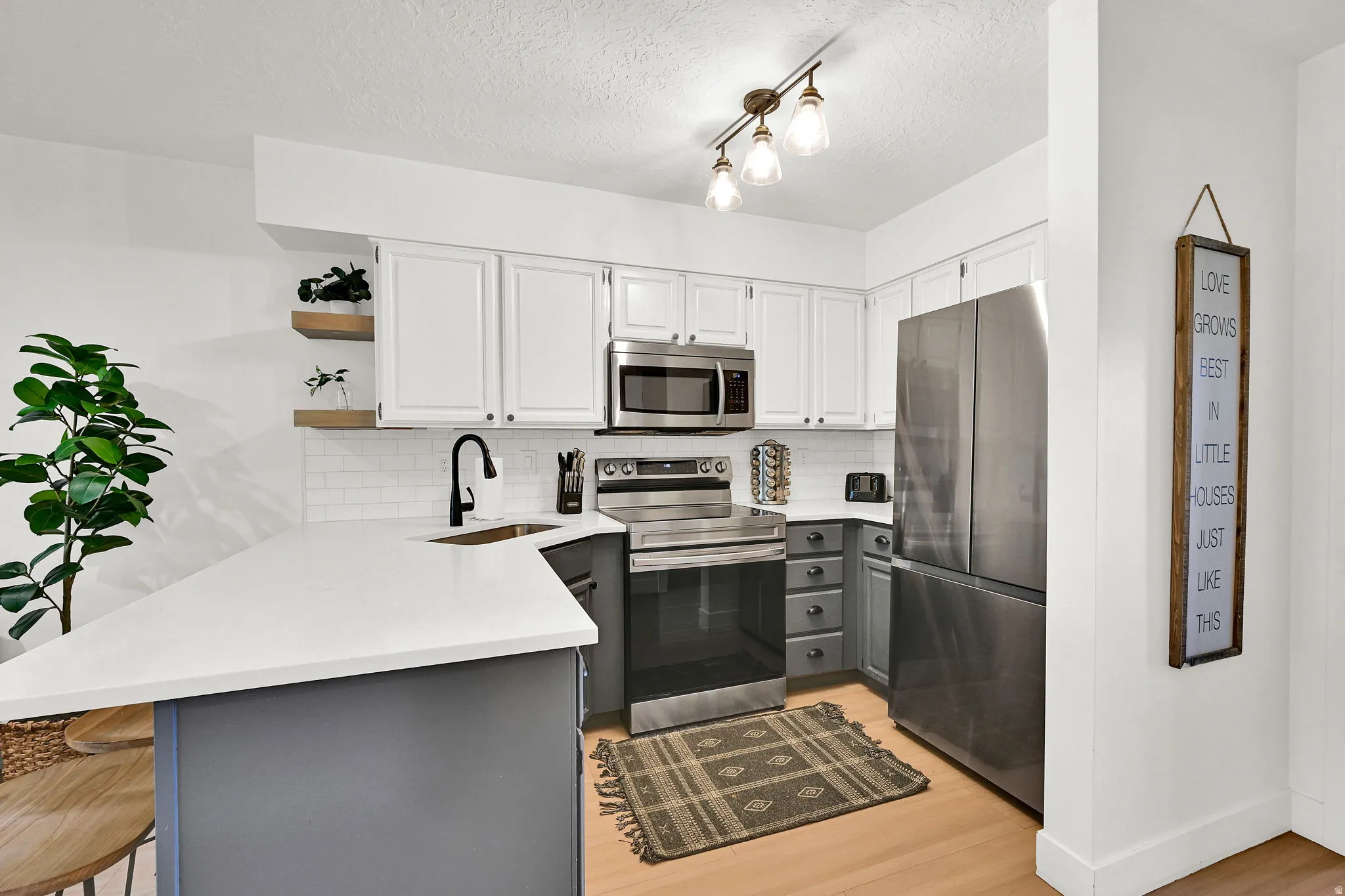 Kitchen featuring a peninsula, a breakfast bar, open shelves, stainless steel appliances, and two-tone cabinets.