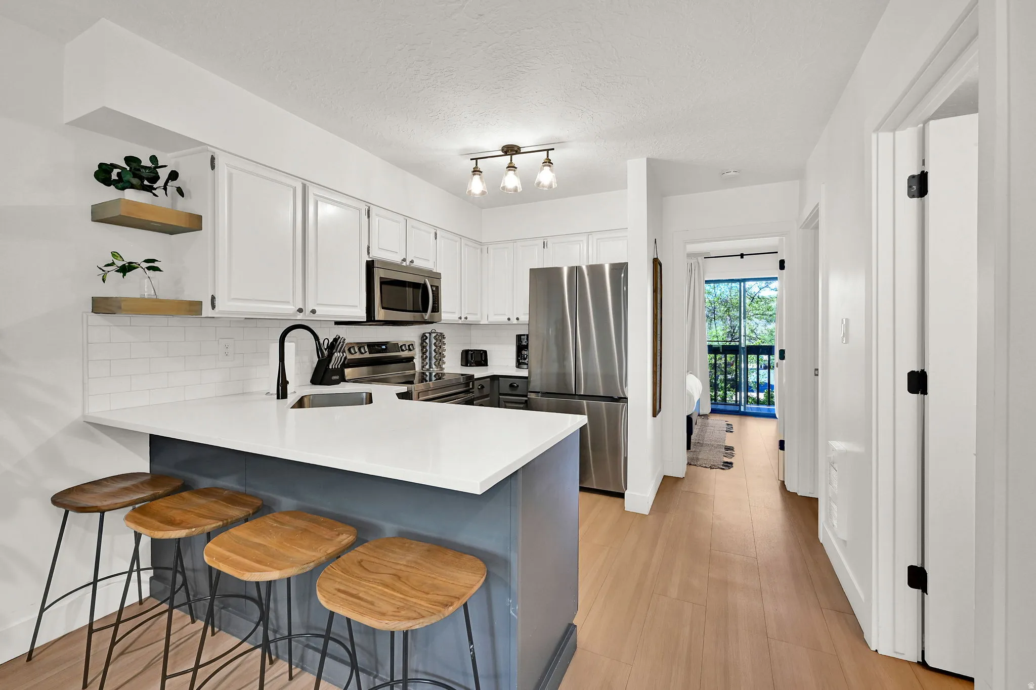 Kitchen featuring a peninsula, a breakfast bar, open shelves, stainless steel appliances, and two-tone cabinets.