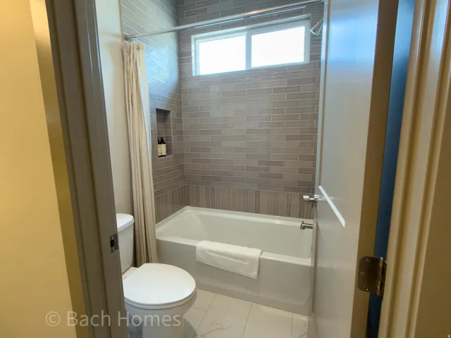 Bathtub with subway tile surround, integrated shower niche, and an upper transom window