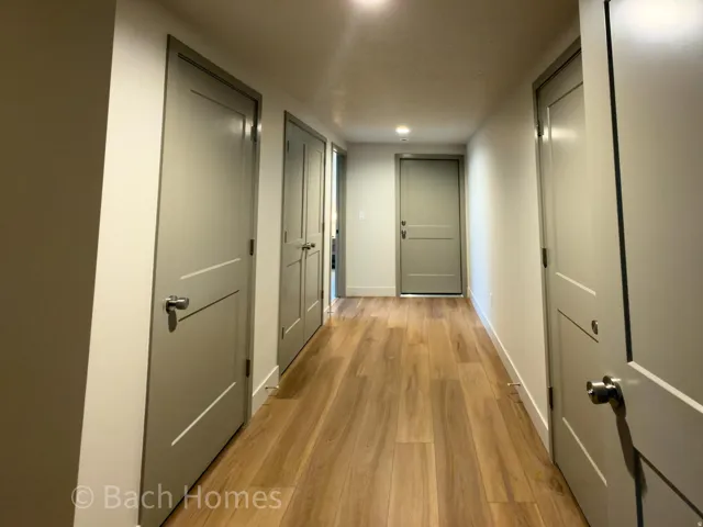 Wood-finish flooring extending through a hallway with recessed lighting, showcasing multiple doors with modern hardware