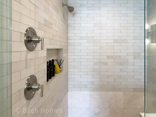 Subway tile shower surround with dual brushed nickel controls, recessed shower niche, and a fixed showerhead