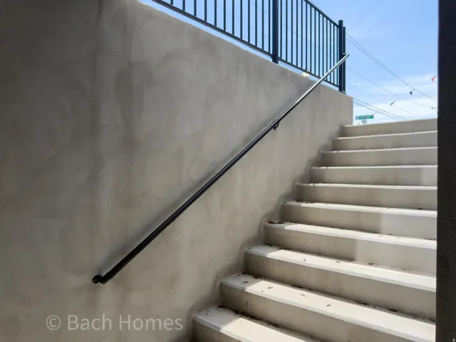 Staircase with concrete treads and risers, a black metal handrail, and a smooth stucco wall