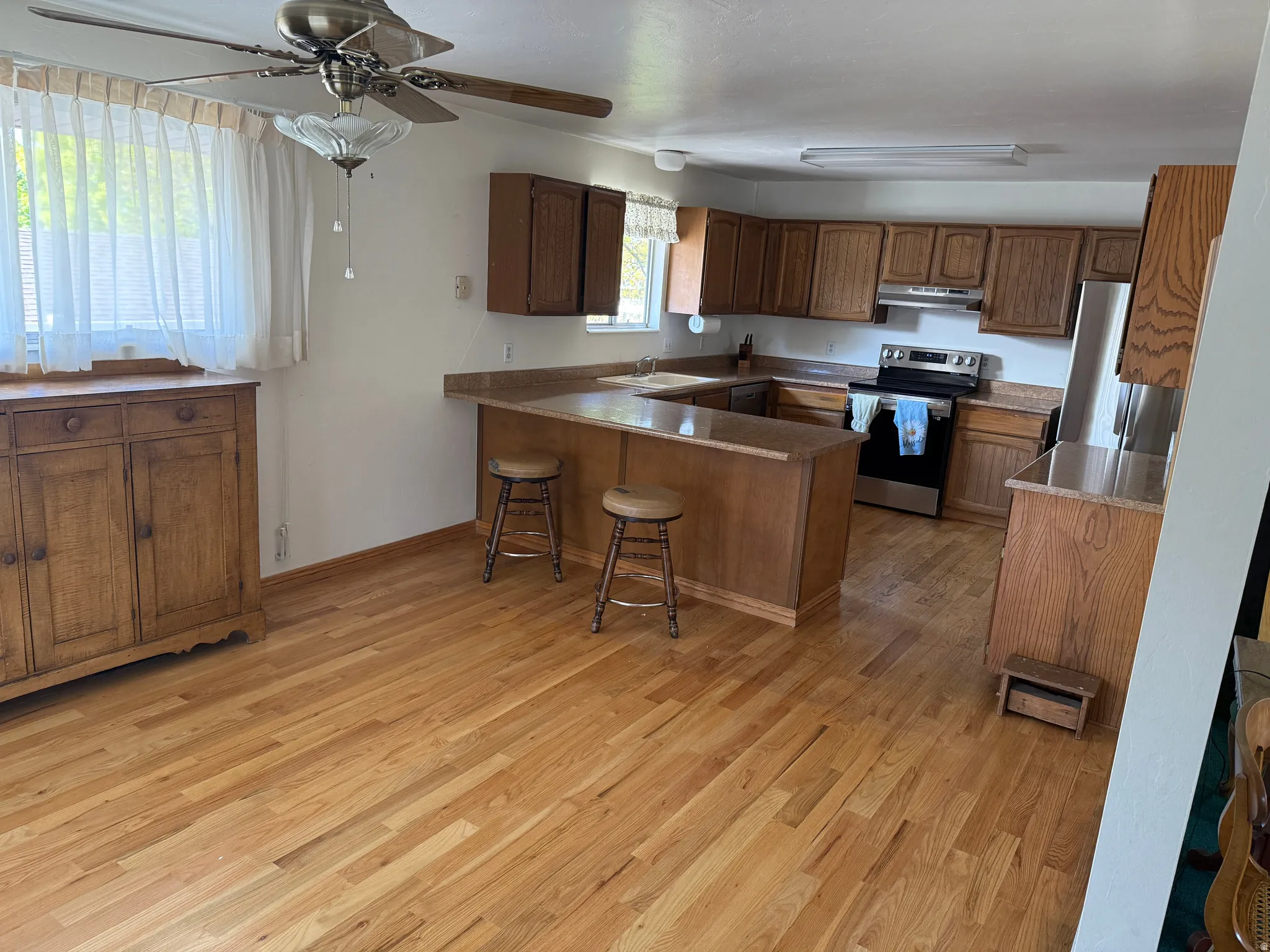 Kitchen with a peninsula, a breakfast bar area, stainless steel appliances, wood finish cabinets, and light wood-style flooring