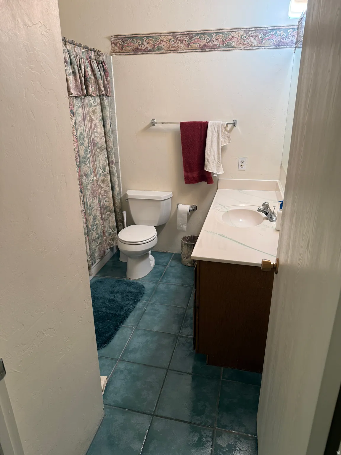 Full bathroom featuring dark tile patterned floors, a shower with curtain, a textured wall, and vanity