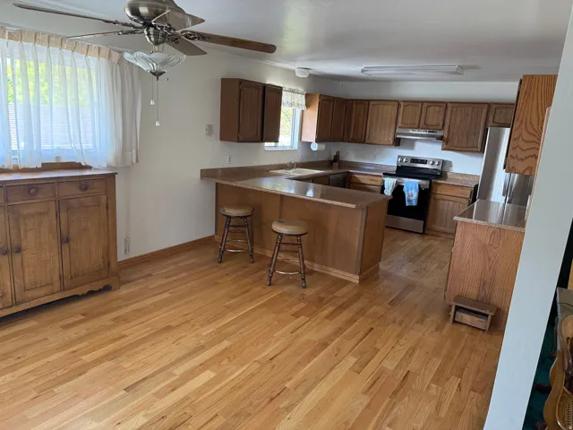 Kitchen with a peninsula, a breakfast bar area, stainless steel appliances, wood finish cabinets, and light wood-style flooring