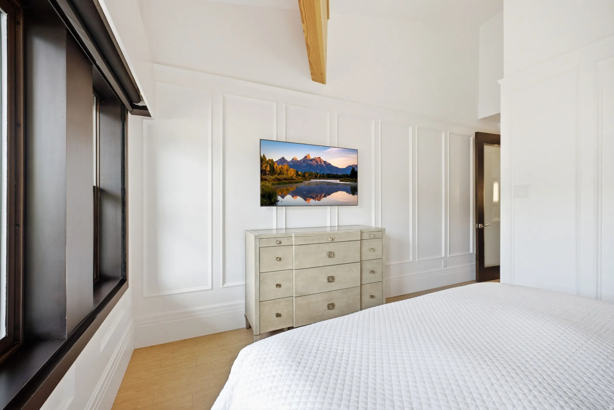 Vaulted ceiling with exposed wood beam, wide plank wood-finish flooring, and elegant wainscoting paneling
