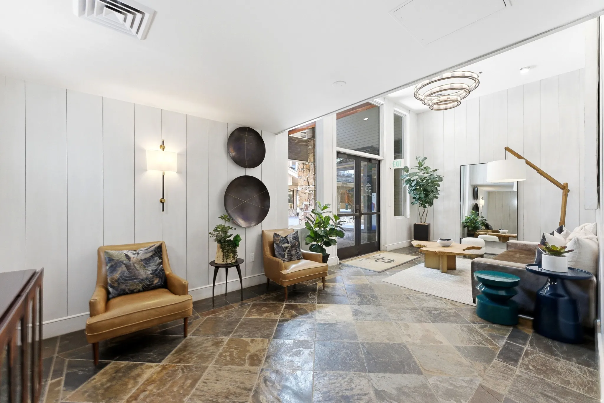 Spacious foyer featuring natural stone tile flooring, vertical plank wall paneling, and a contemporary multi-tier chandelier