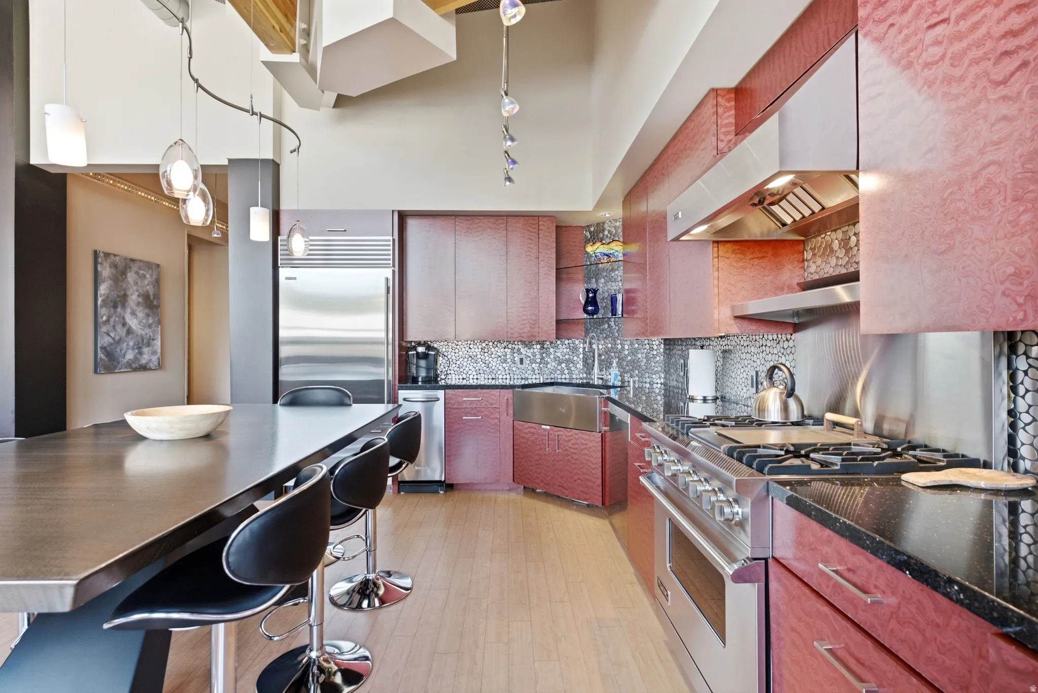 Gourmet kitchen featuring deep red cabinetry, black granite countertops, a built-in stainless steel oven range, a stainless steel farmhouse sink, and a mosaic tile backsplash