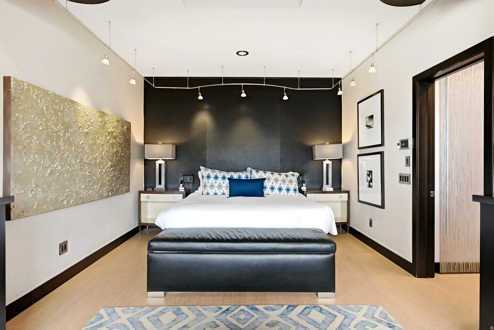 Recessed and track lighting illuminate a feature wall with a dark textured finish, complemented by light wood-finish flooring