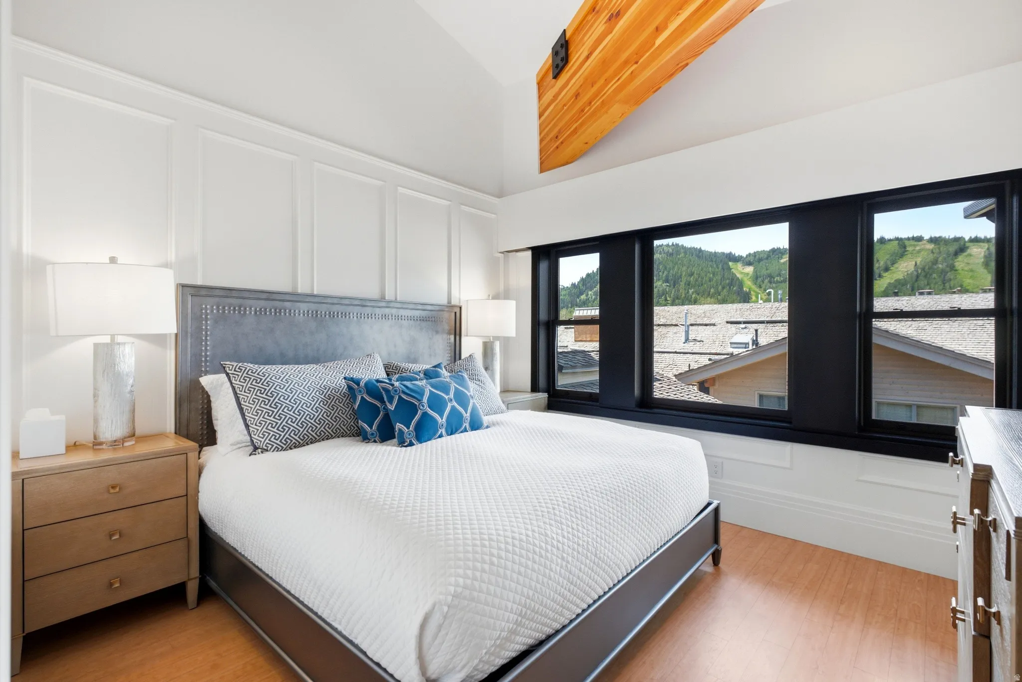 Vaulted ceiling with an exposed wood beam, black-framed windows, and light wood-finish flooring