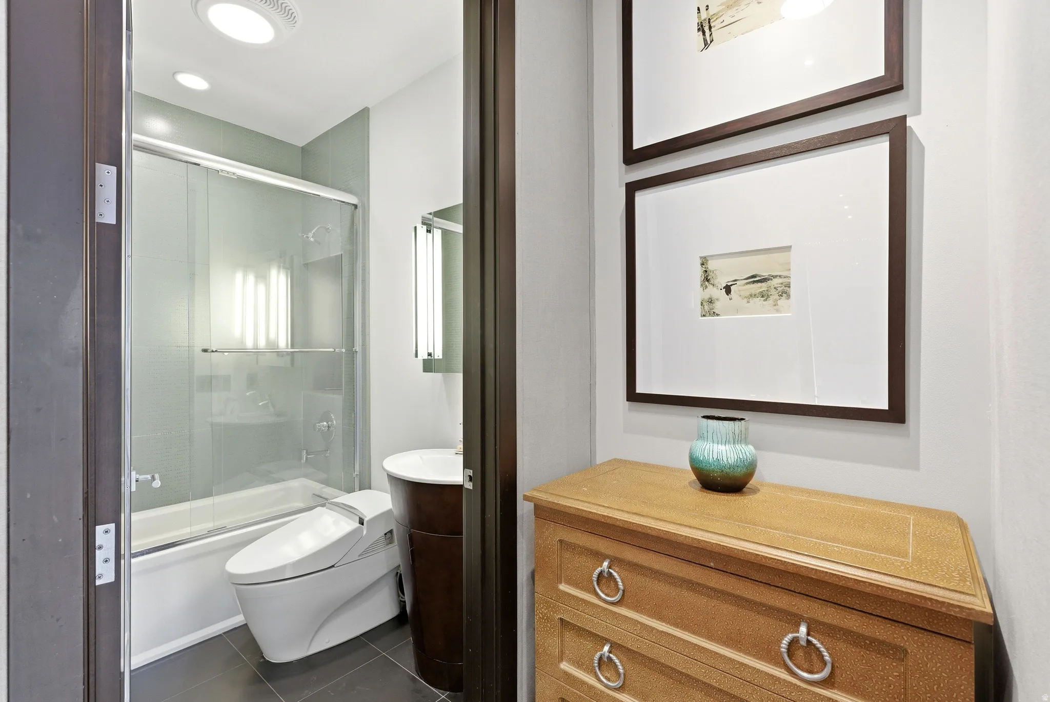 Modern bathroom featuring a sliding glass shower door over the tub, contemporary vanity with vessel sink, and large format floor tiles