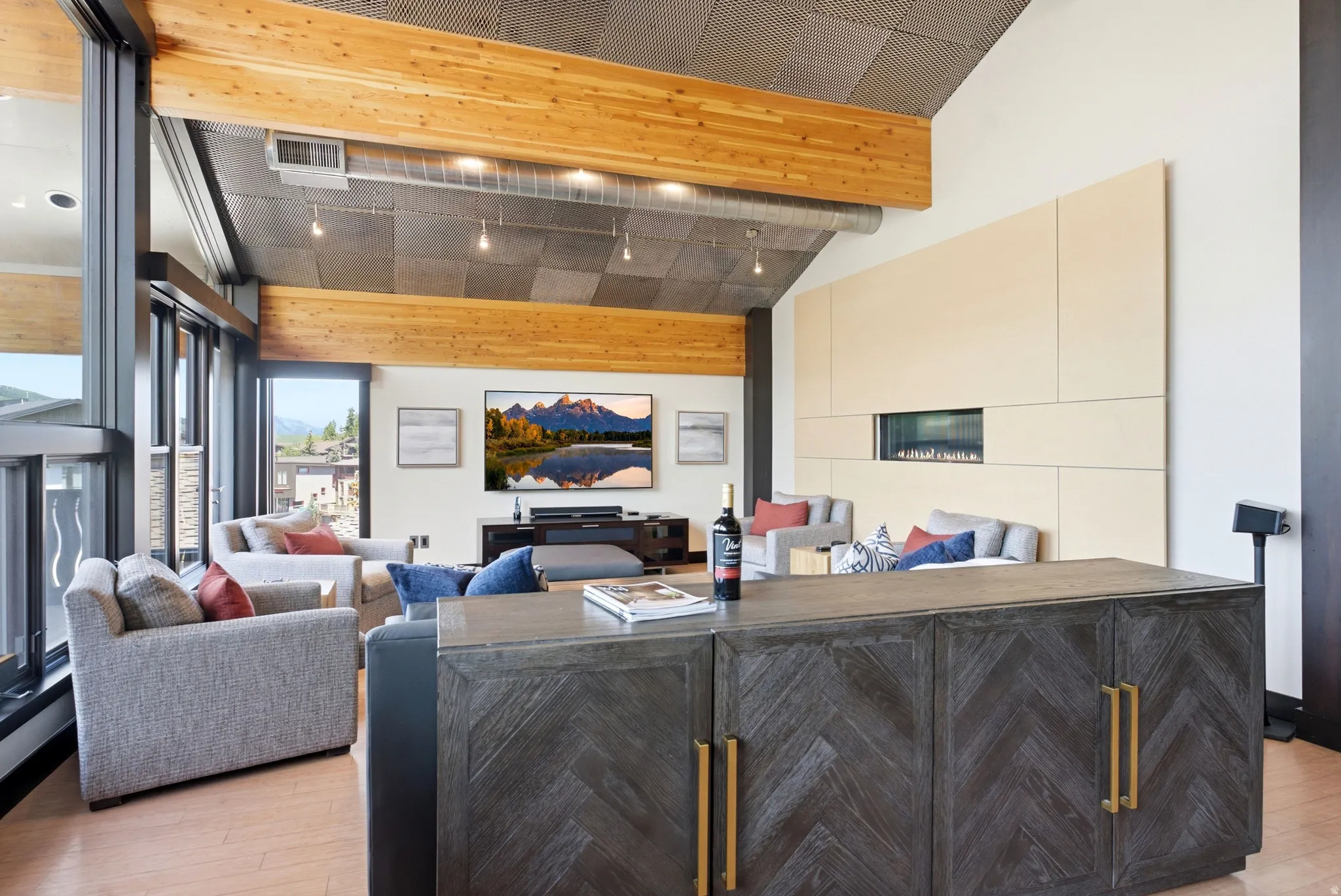 Spacious living area featuring floor-to-ceiling windows, wood-finish flooring, exposed wood beams, and a modern linear fireplace integrated into a panel wall