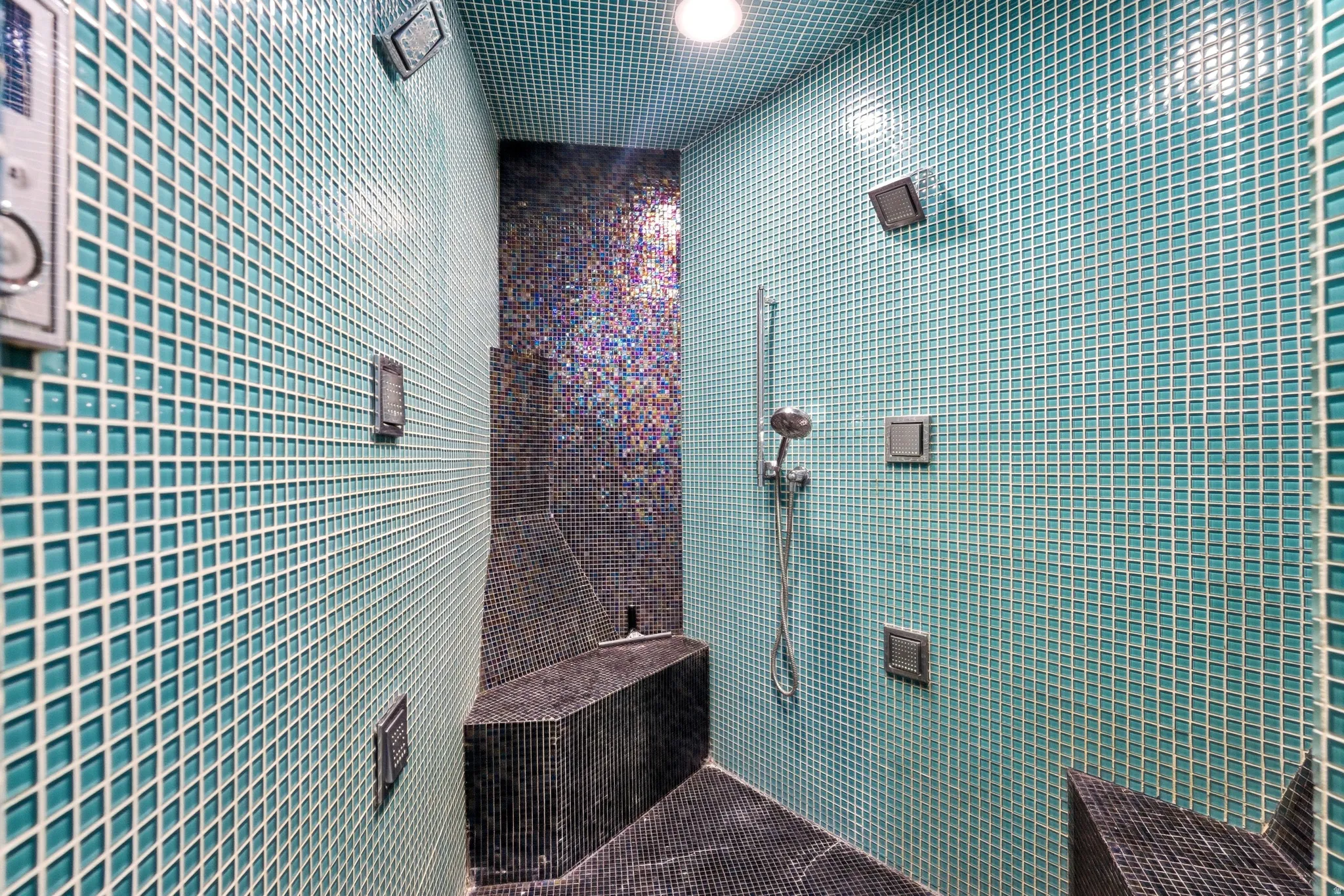 Shower enclosure featuring full-height teal mosaic tiling, a built-in bench, and a handheld shower fixture