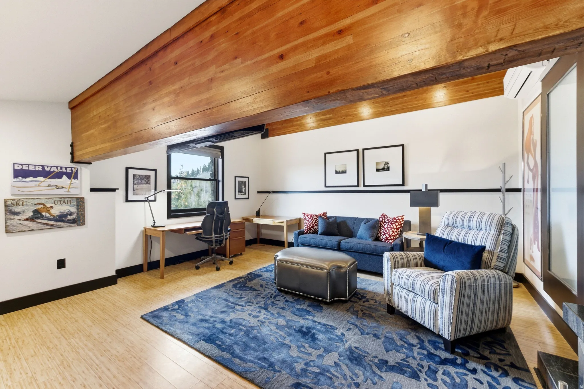 Room featuring wood-finish flooring, exposed wood beam ceiling, white walls with a black chair rail, and multiple windows