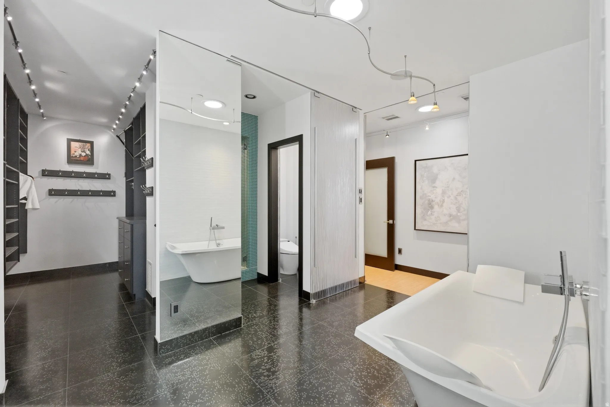 Contemporary bathroom featuring a freestanding soaking tub, dark large-format tile flooring, a walk-in shower with a tile surround, and an adjacent walk-in closet with built-in shelving
